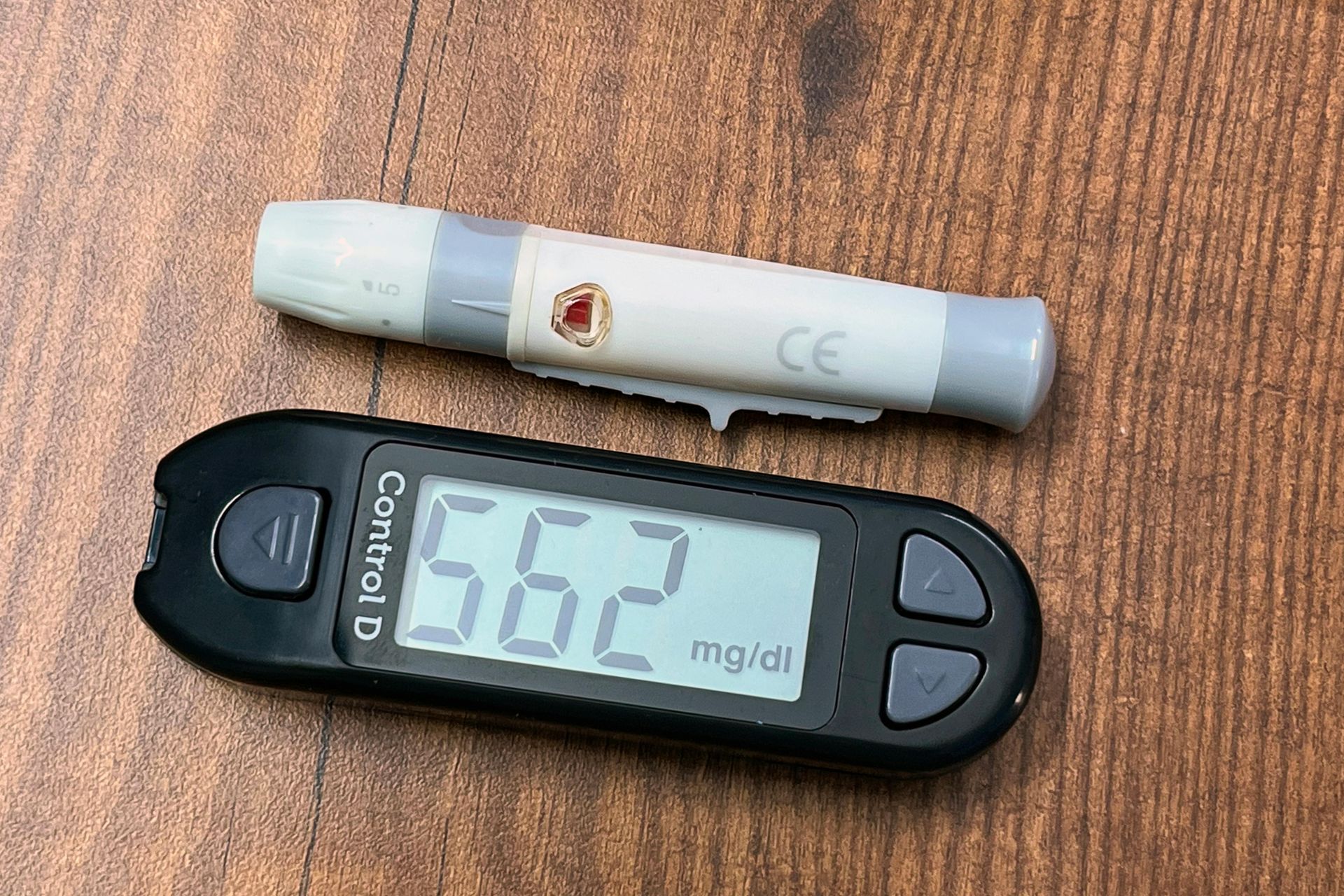 Blood glucose meter showing 66 mg/dL beside a test strip on a wooden surface