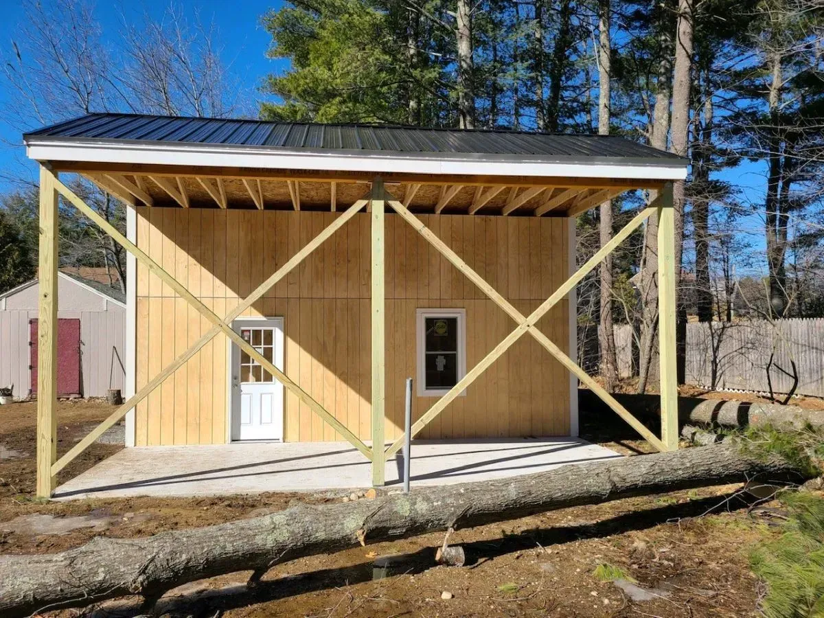 A small wooden building with a black roof is being built in the woods.