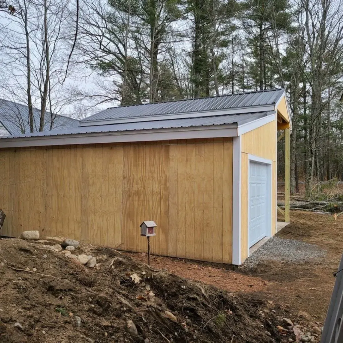A wooden garage with a metal roof is sitting on top of a dirt hill.