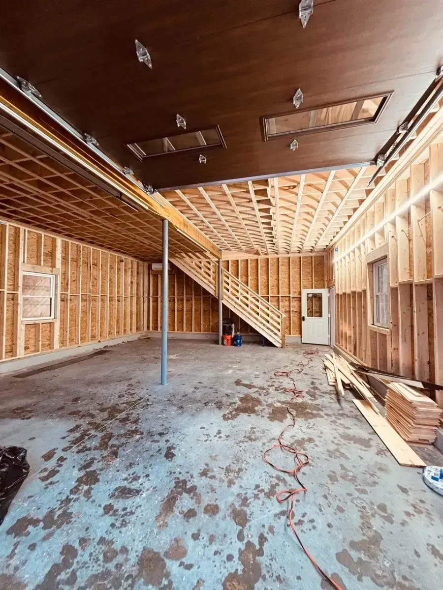 Interior view of a garage under construction with wooden framing, cement floor, and a staircase.