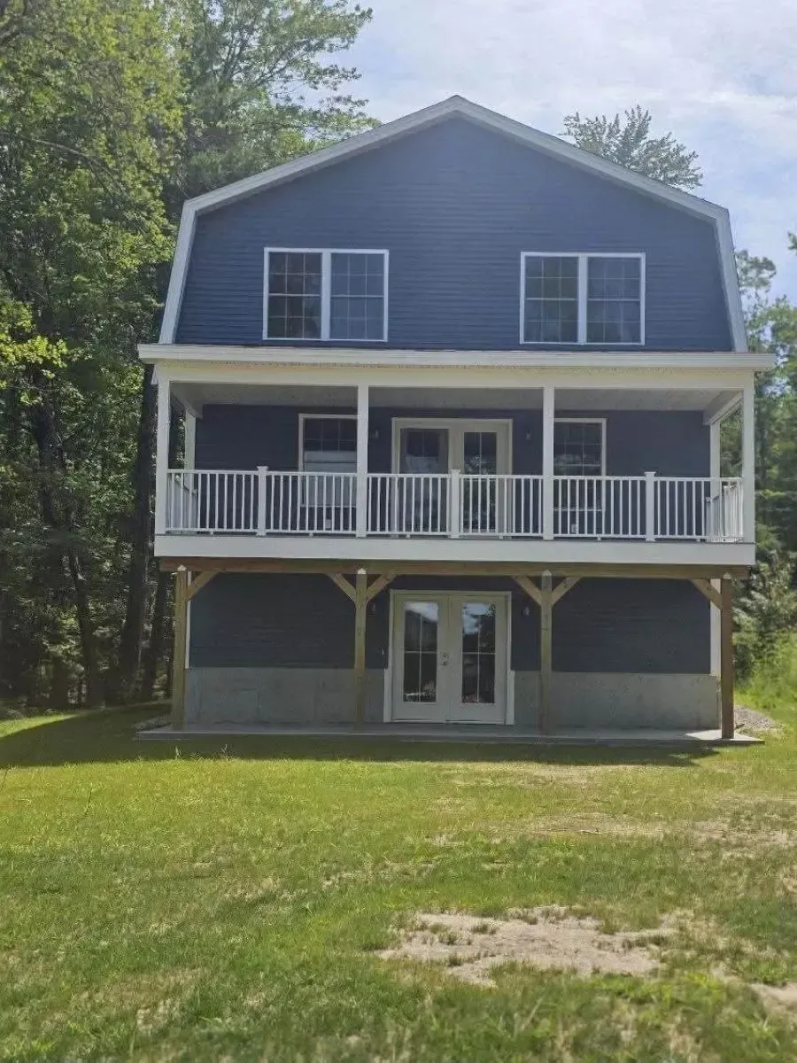 Blue two-story house with white trim, front porch, and surrounding trees and lawn