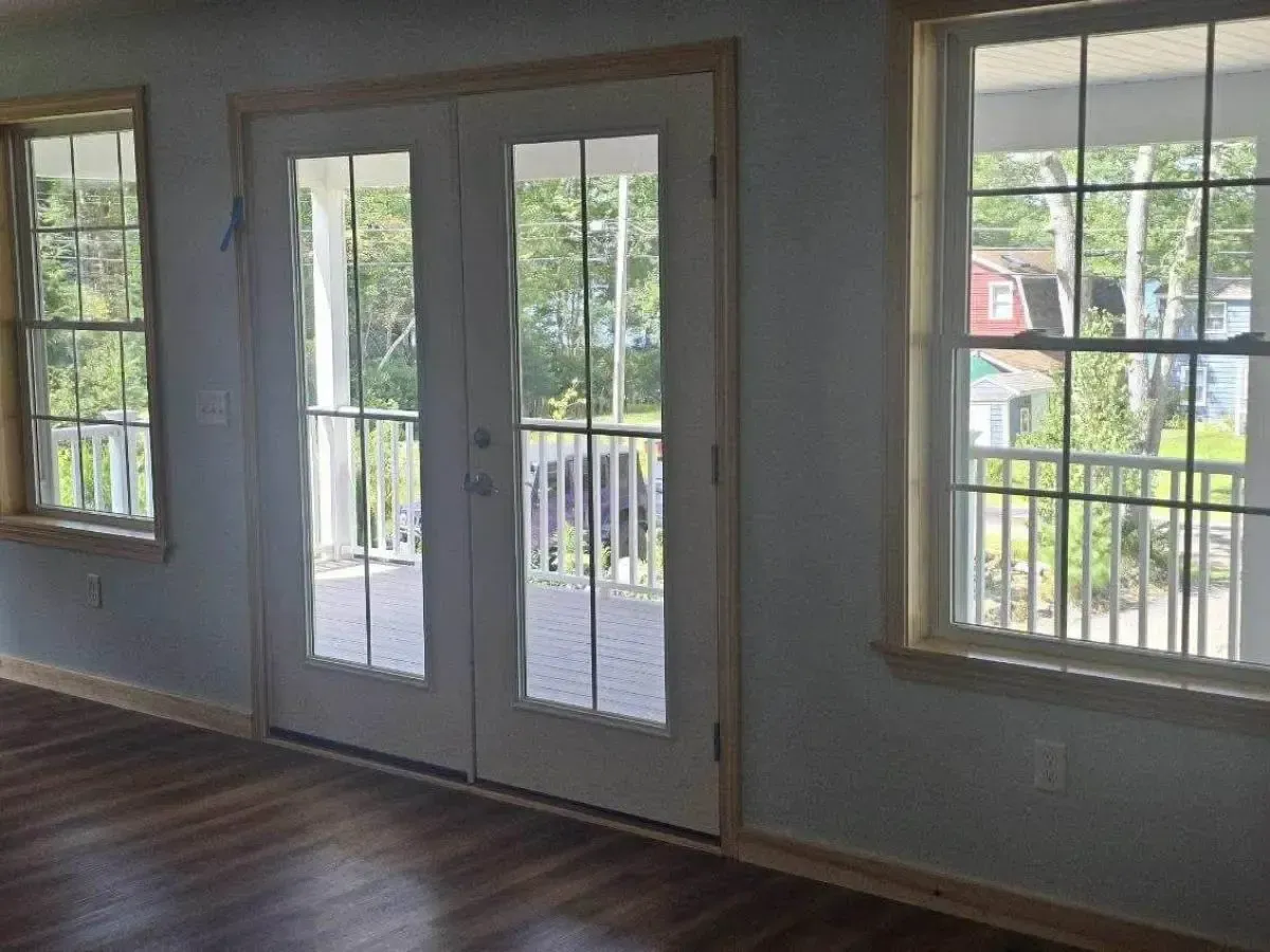 Empty room with hardwood floors, French doors, and large windows overlooking a balcony.