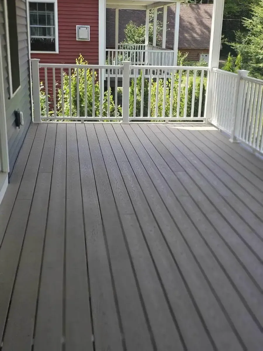 Empty gray wooden deck with white railing overlooking a backyard and red house.