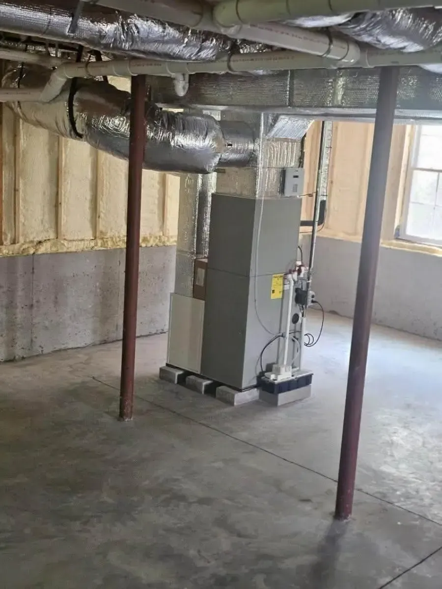 Basement utility room with a furnace, exposed ductwork, and support posts on a concrete floor