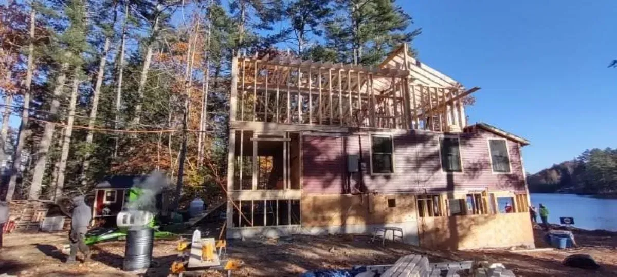 A house is being built on the shore of a lake surrounded by trees.