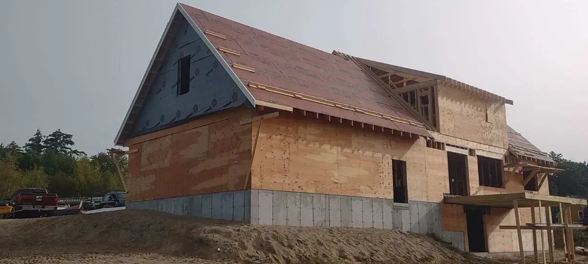 A house under construction with a red roof is sitting on top of a dirt hill.