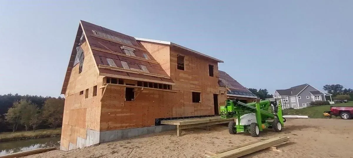 A green forklift is moving a brick house on a dirt road.