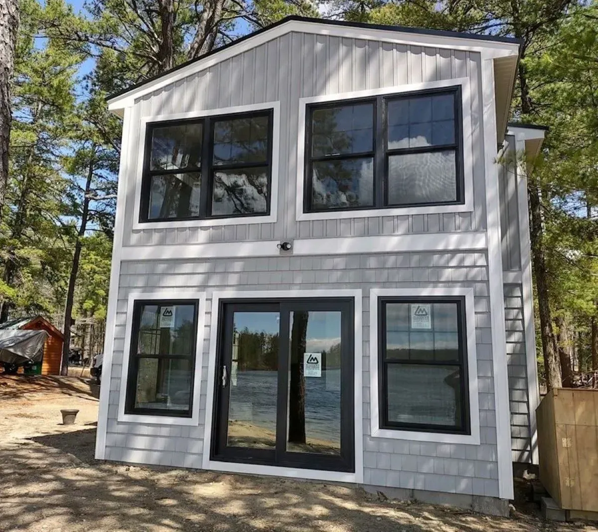 A small house with a lot of windows and doors is surrounded by trees.