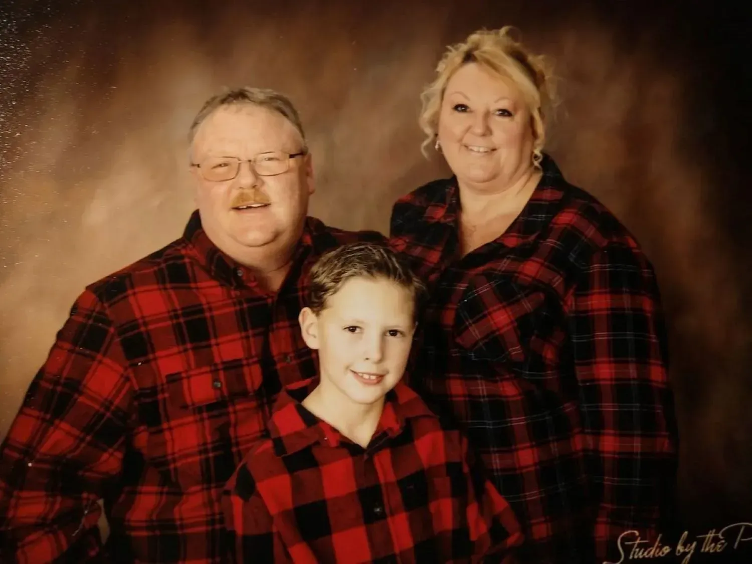 A man and woman are posing for a picture with a boy in a plaid shirt