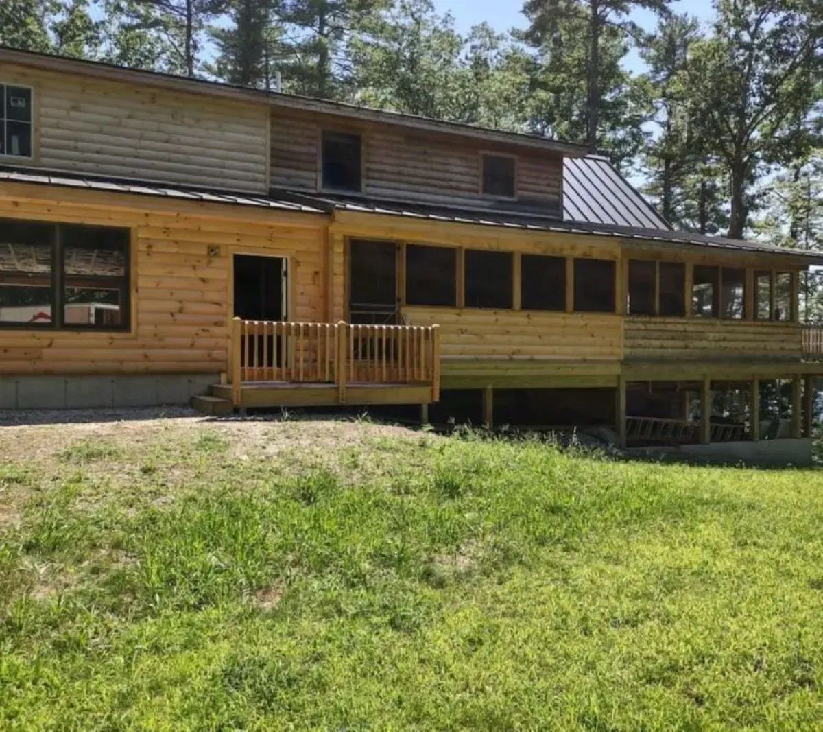 A large wooden house with a large deck is surrounded by trees