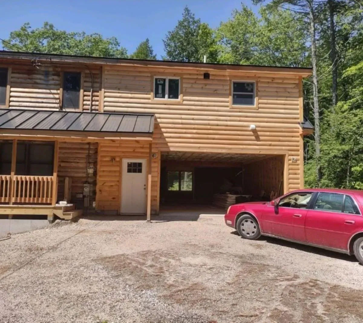 A red car is parked in front of a wooden house