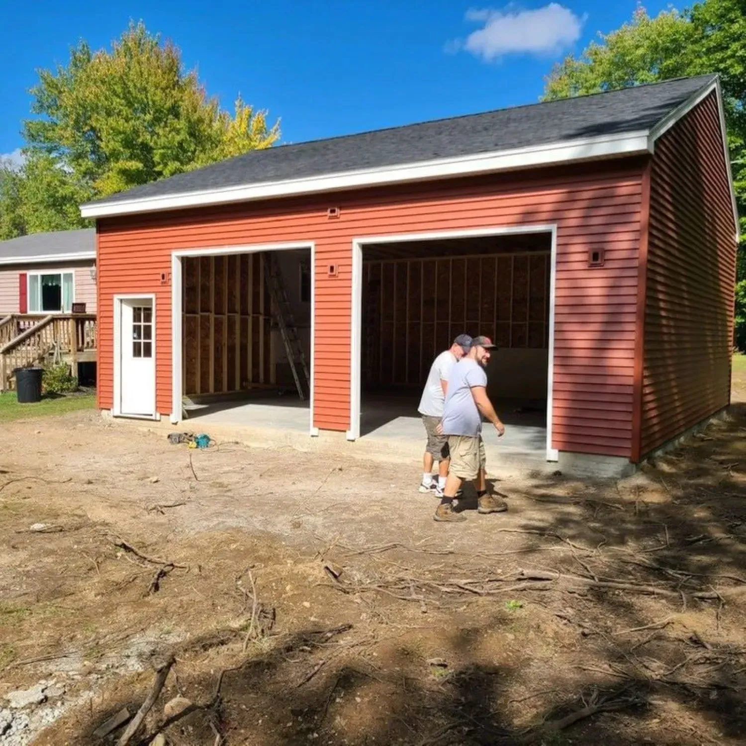 Two men are standing in front of a red garage