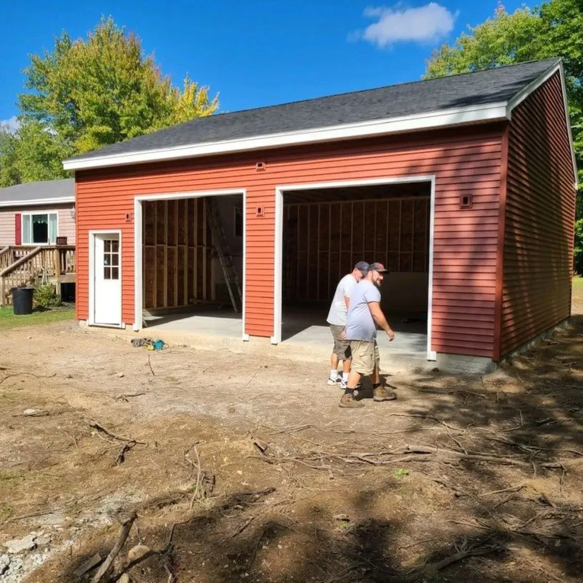 Two men are standing in front of a red garage under construction