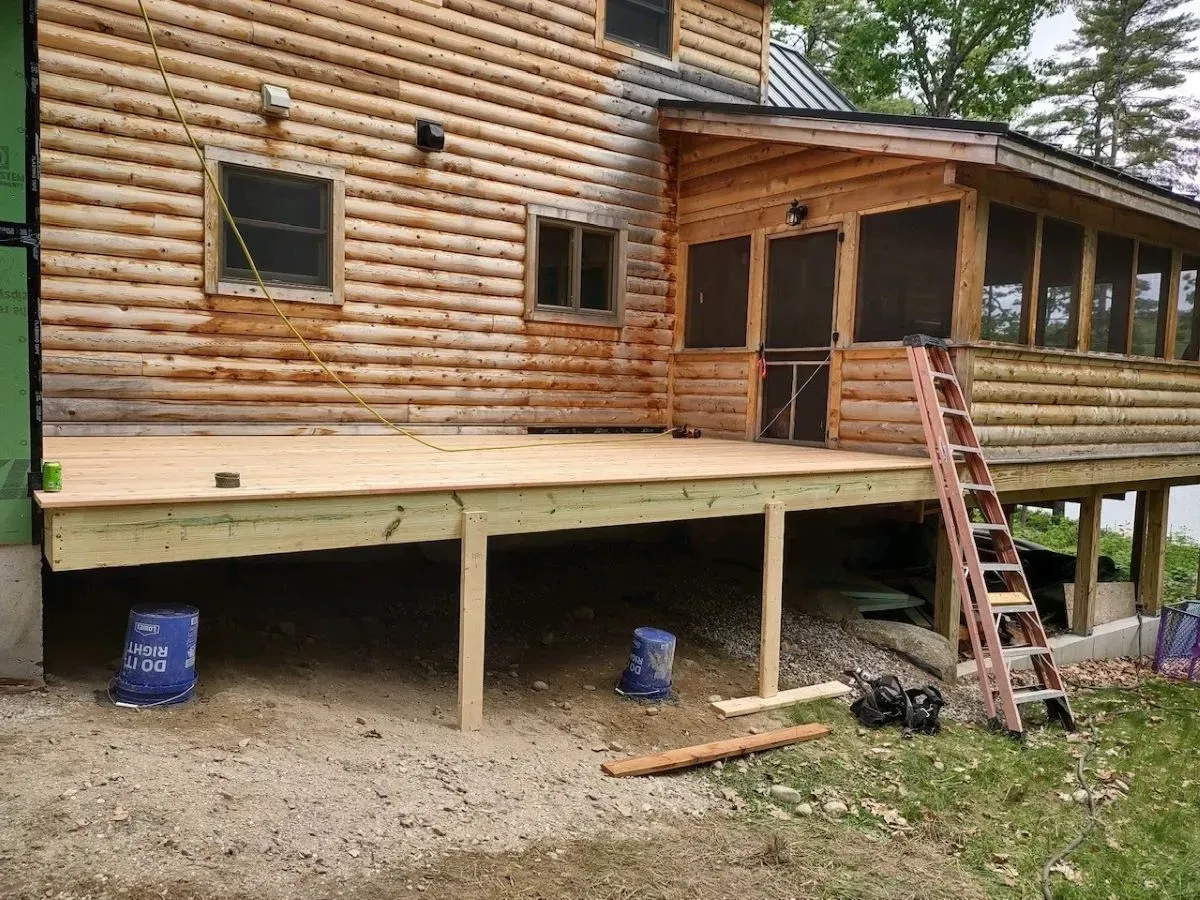 A wooden deck is being built in front of a log cabin.