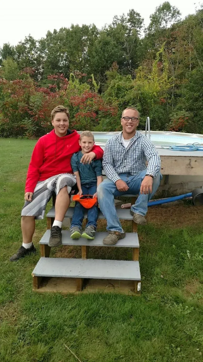 Three people are sitting on steps next to a pool.