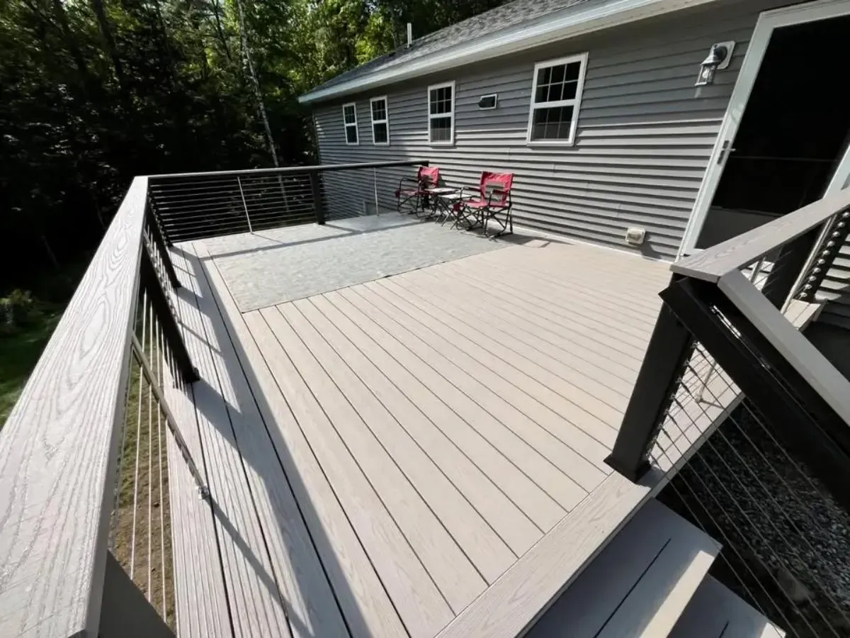 Spacious gray backyard deck with black railings and two pink chairs beside a house