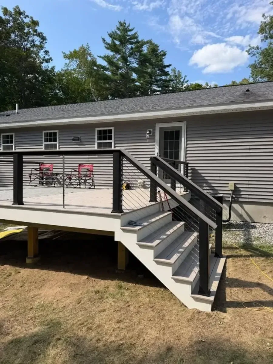 House exterior with raised deck, gray siding, black railing, and stairs leading to the yard