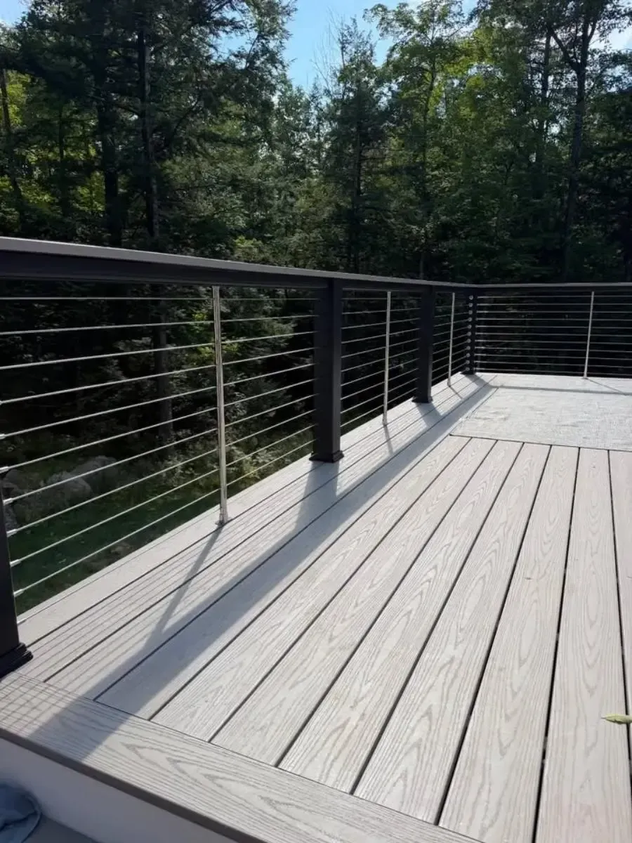 Wooden deck with black cable railing overlooking dense green forest on a sunny day