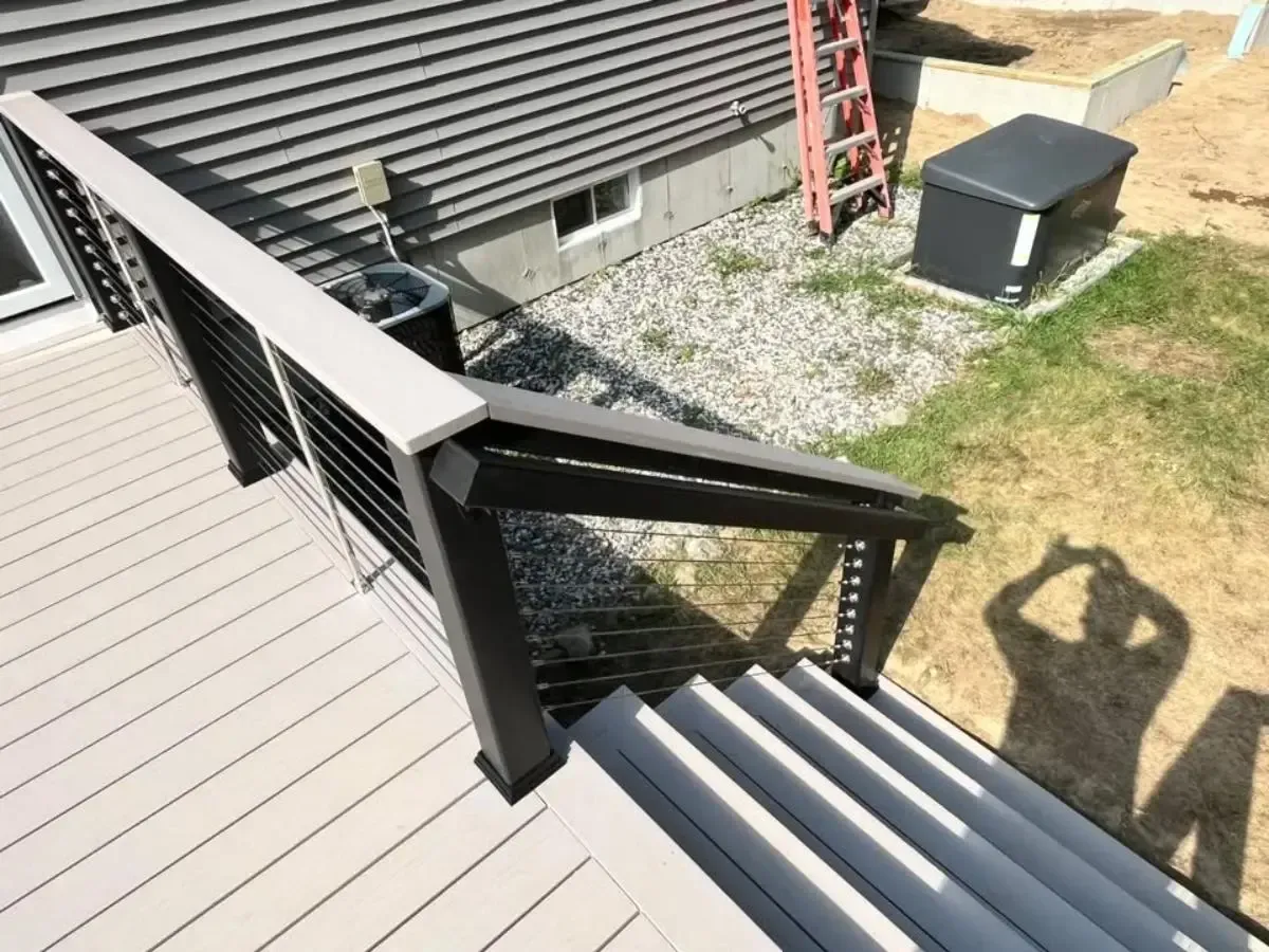 Outdoor stairs with black railing beside a house, viewed from above, with gravel, grass, and ladder nearby