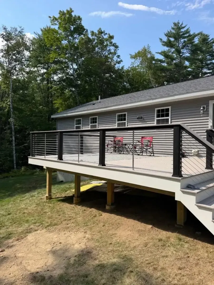 House with elevated deck and railing, two red chairs on the porch, surrounded by trees