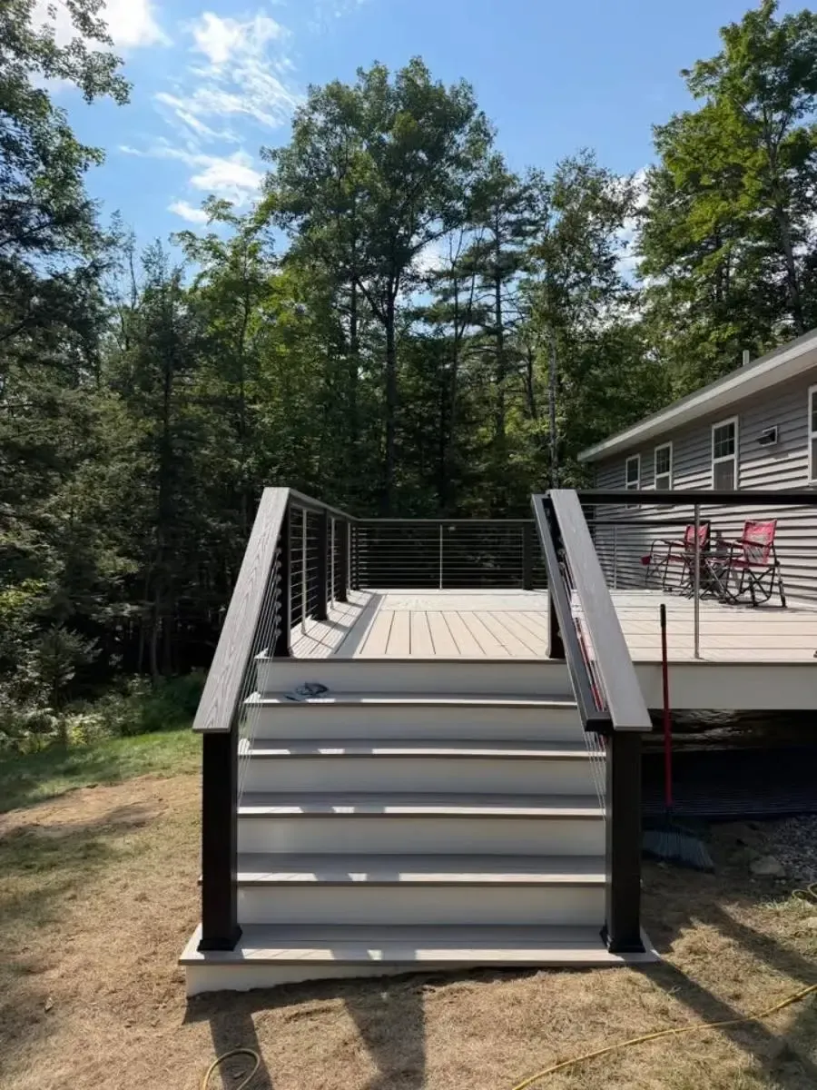 Backyard deck with wide gray stairs, black railings, and patio chairs beside a house