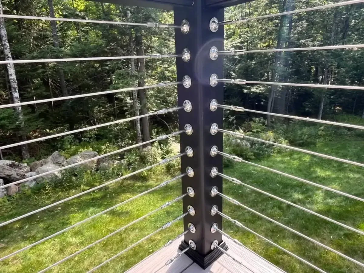 Metal railing corner with horizontal cables overlooking a green wooded area