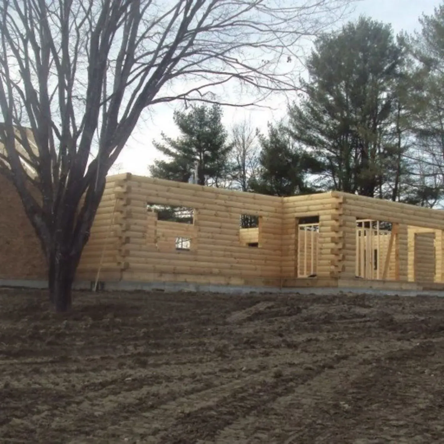 A log cabin is being built in a field with trees in the background