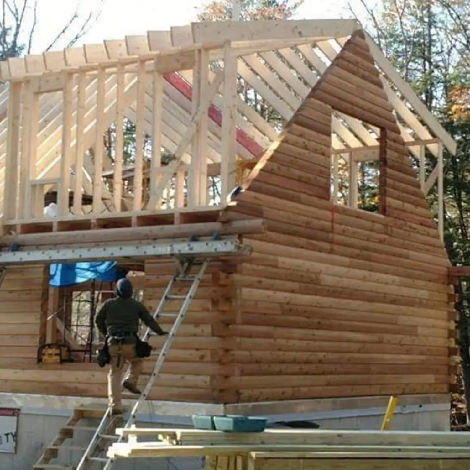 A man standing on a ladder in front of a log cabin under construction