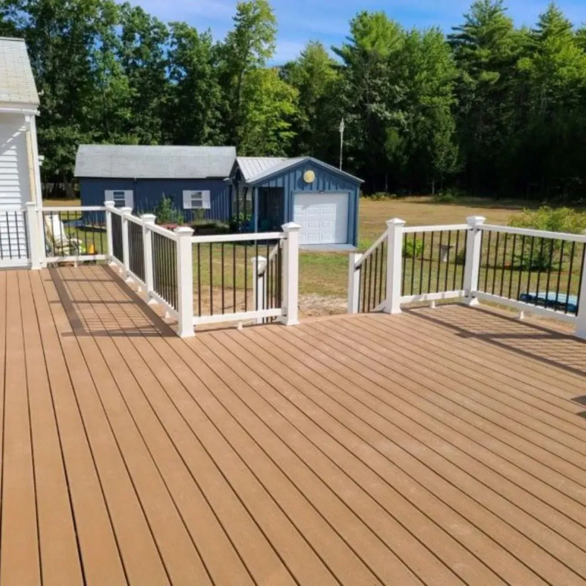 A wooden deck with a white railing and a blue garage in the background