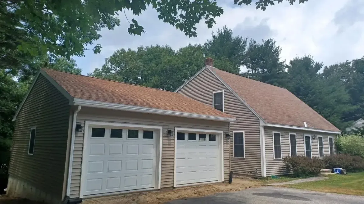 House with attached two-car garage, tan siding, and a red shingle roof under trees