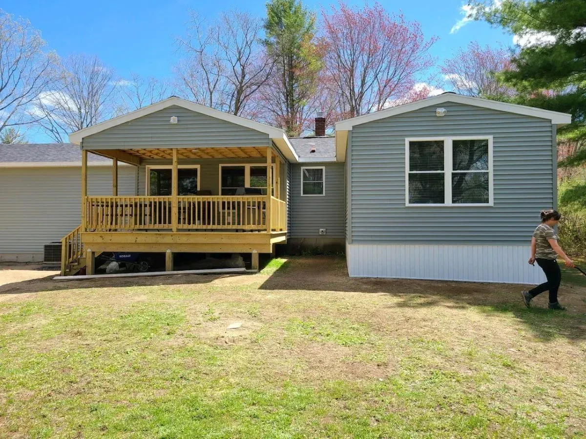 A woman is walking in front of a mobile home with a porch.