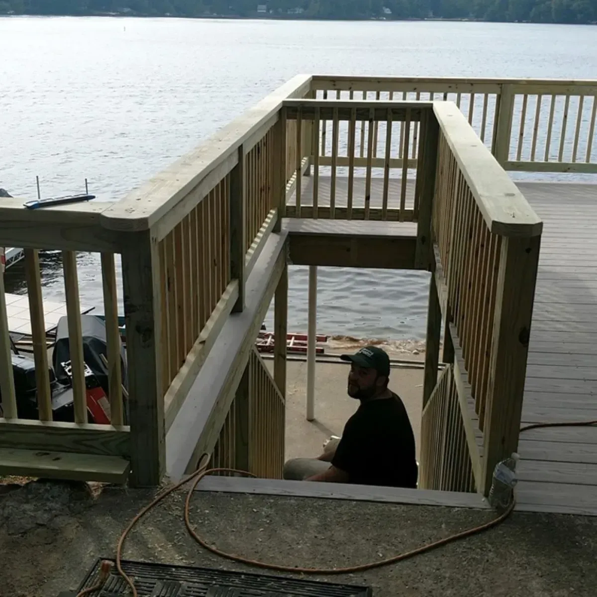 A man sits on the steps of a wooden deck overlooking a body of water
