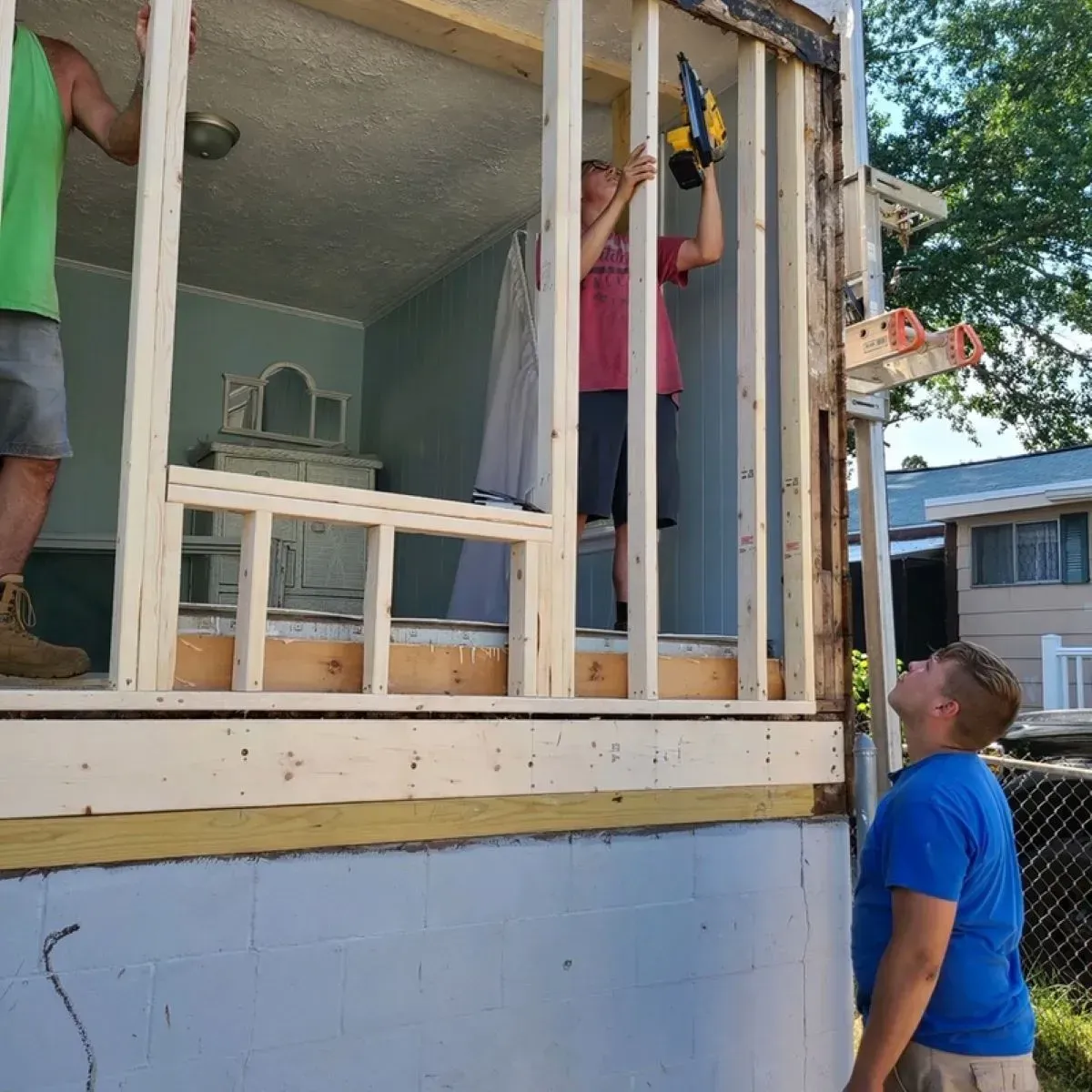 A man in a blue shirt stands in front of a house being built