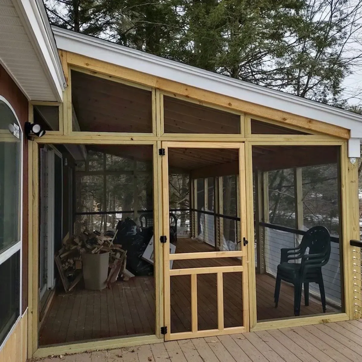 A screened in porch with chairs and trees in the background