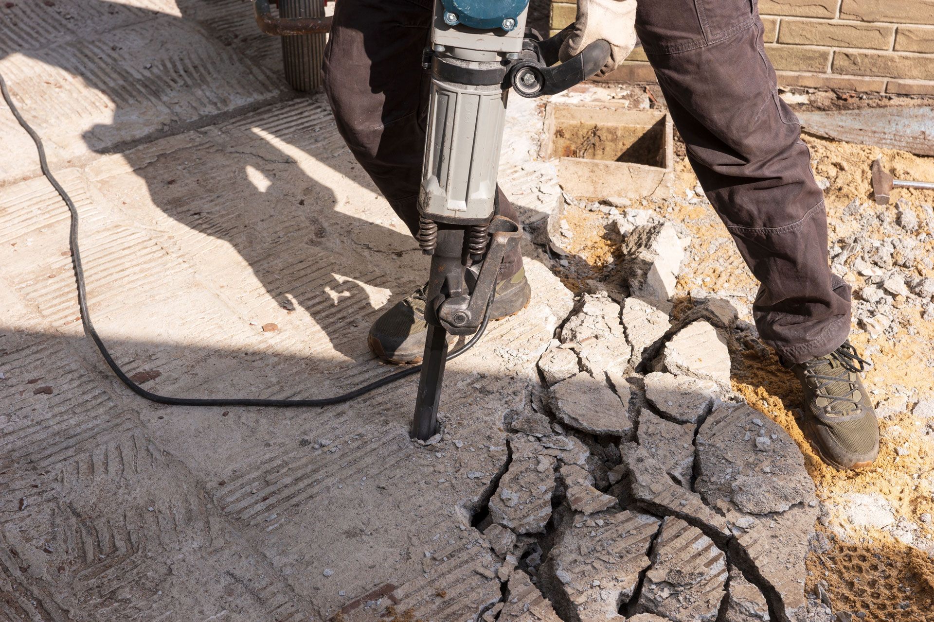 Worker using a jackhammer to break cracked concrete on a street or sidewalk