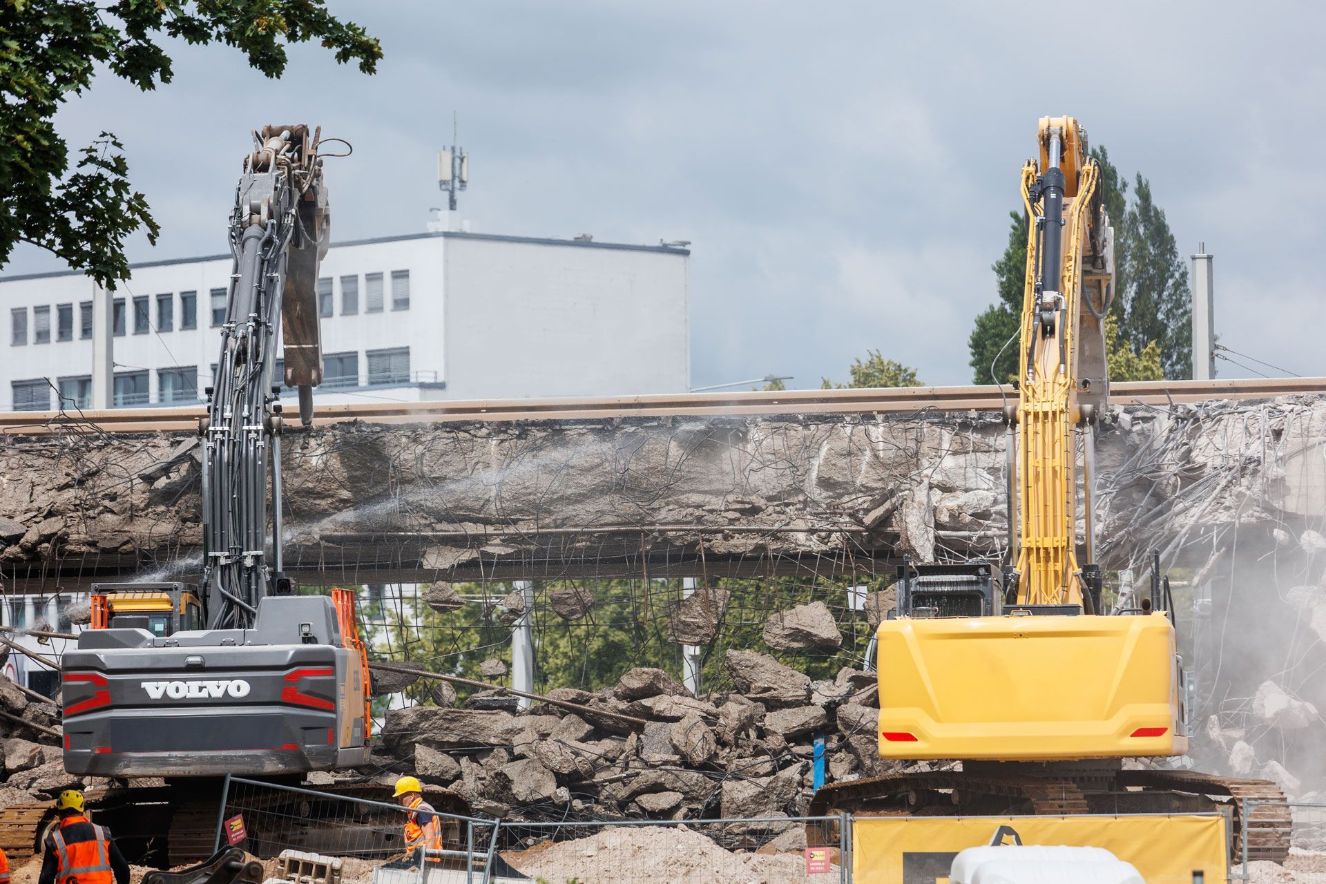 Demolition site with two excavators clearing rubble beside a damaged concrete wall.