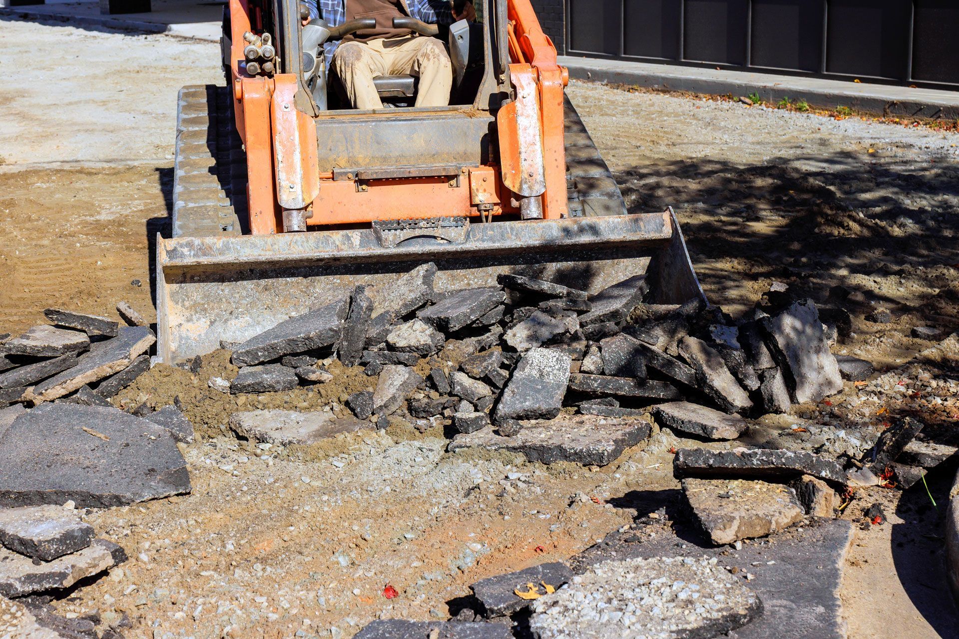 Orange skid steer pushing broken asphalt and debris on a road repair site