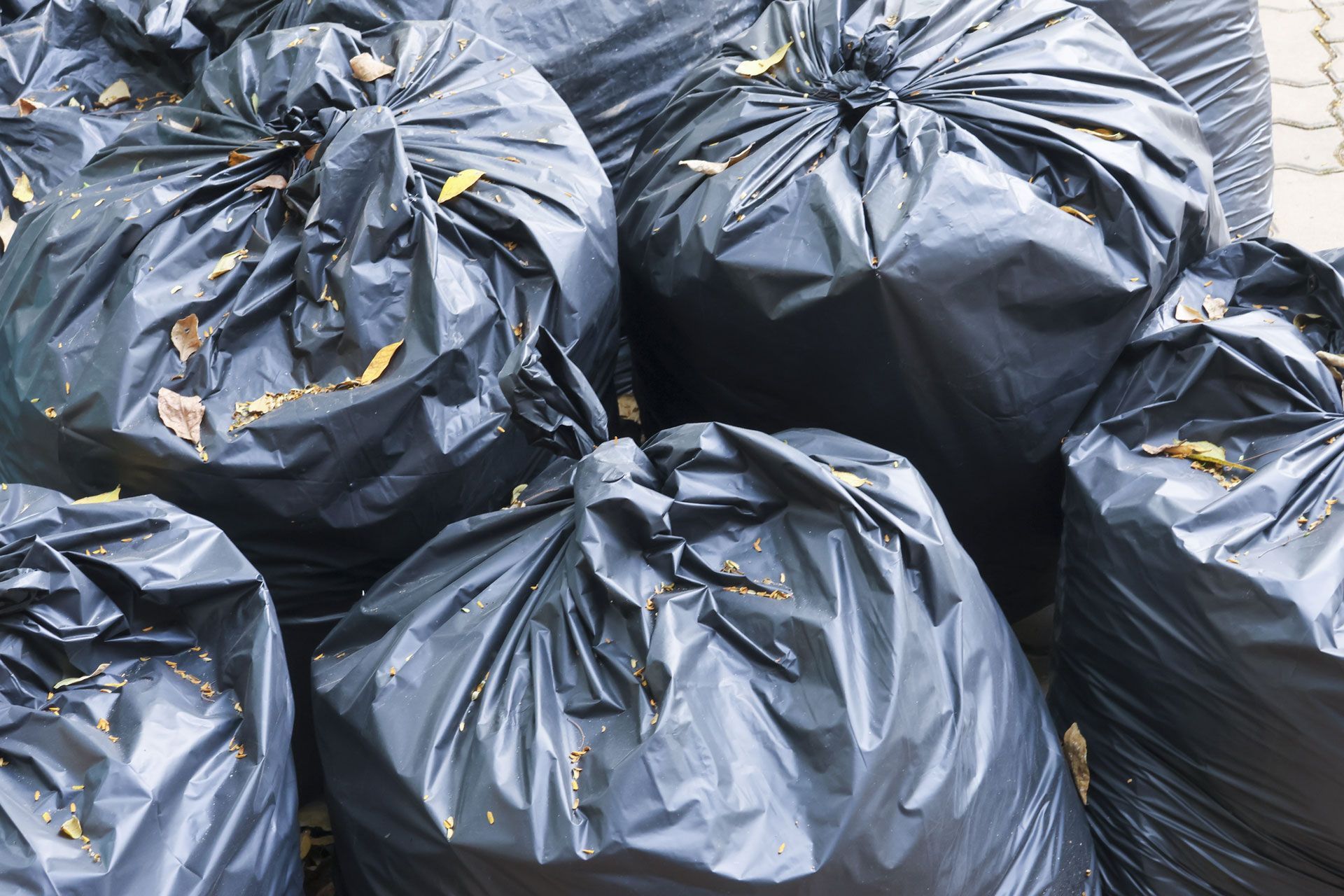 Piles of black garbage bags stacked outdoors on pavement