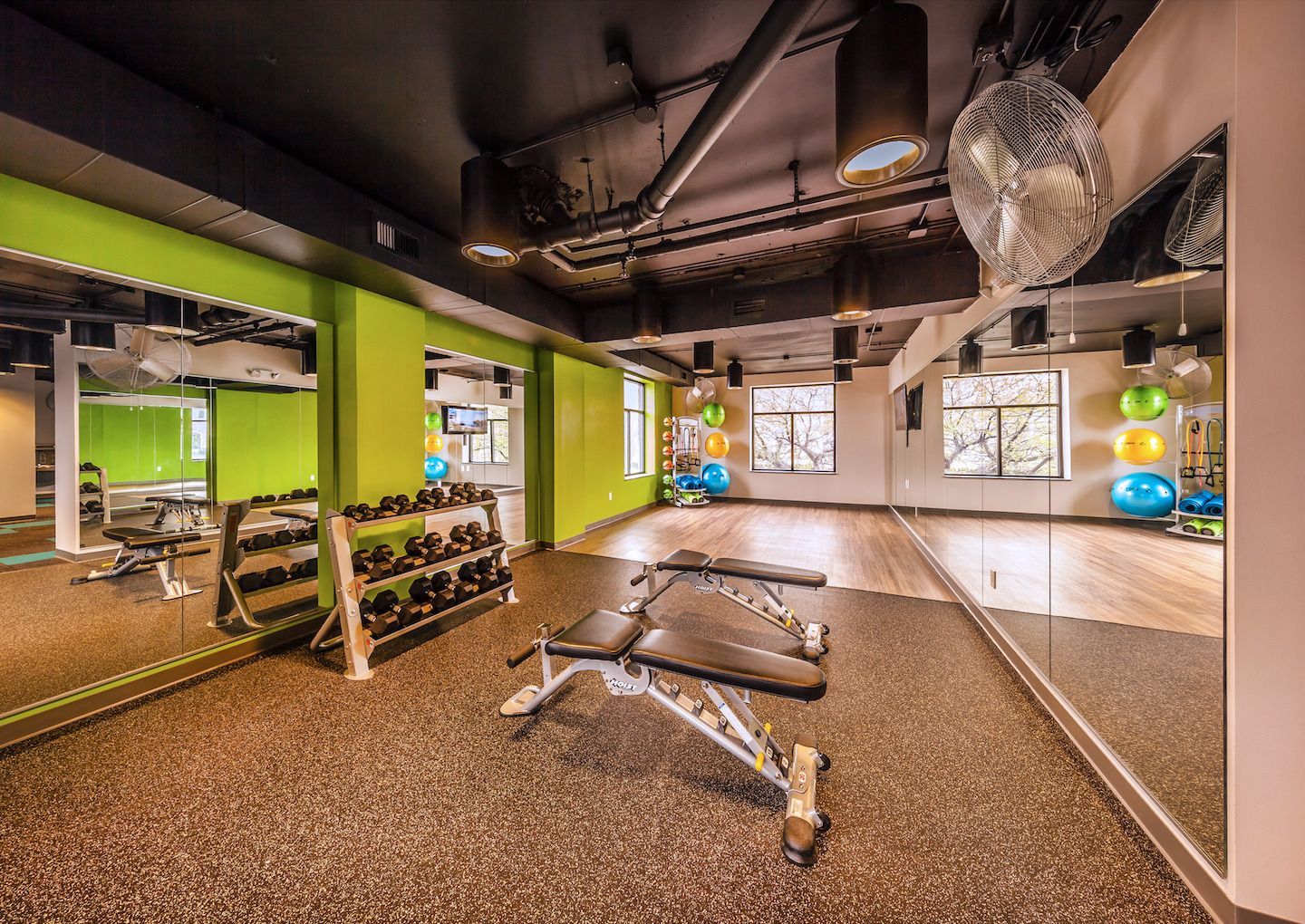 A gym with a bench , dumbbells , and mirrors.