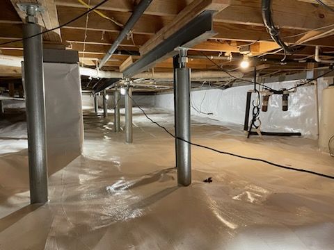 Crawl space with support beams, insulation, and columns. White plastic covers the floor and walls.