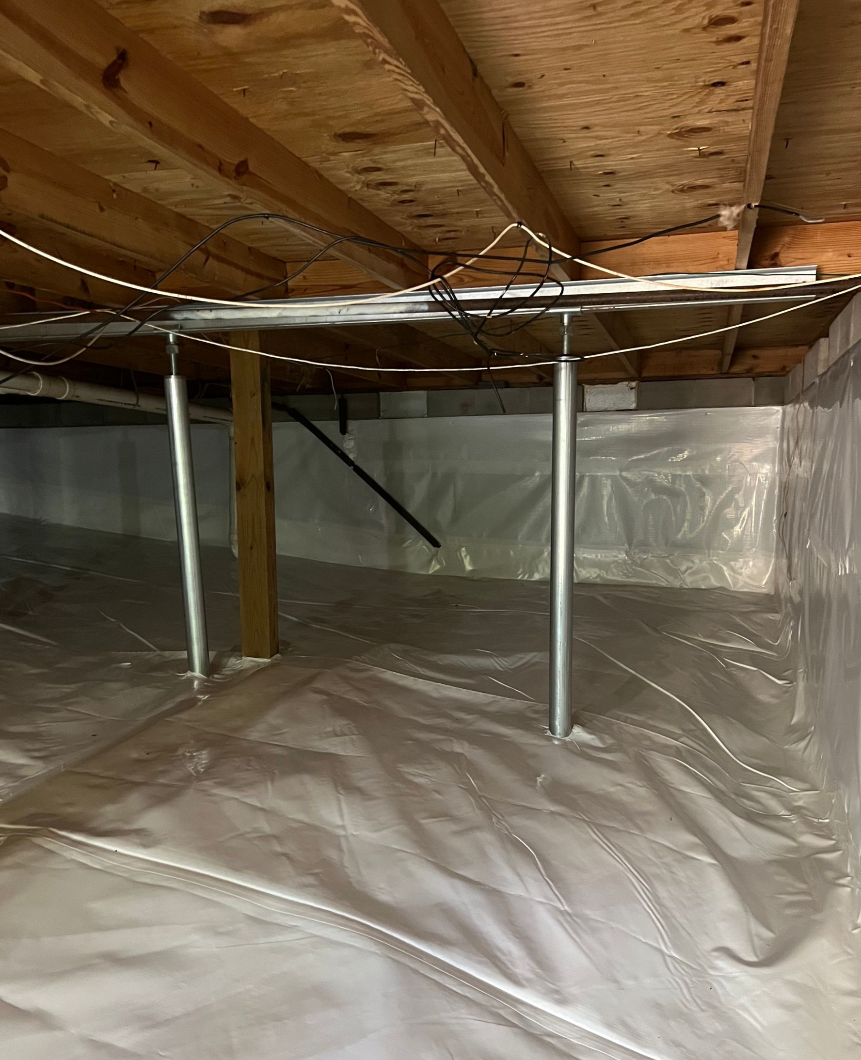 Crawl space under wooden floor with silver vapor barrier and metal support posts