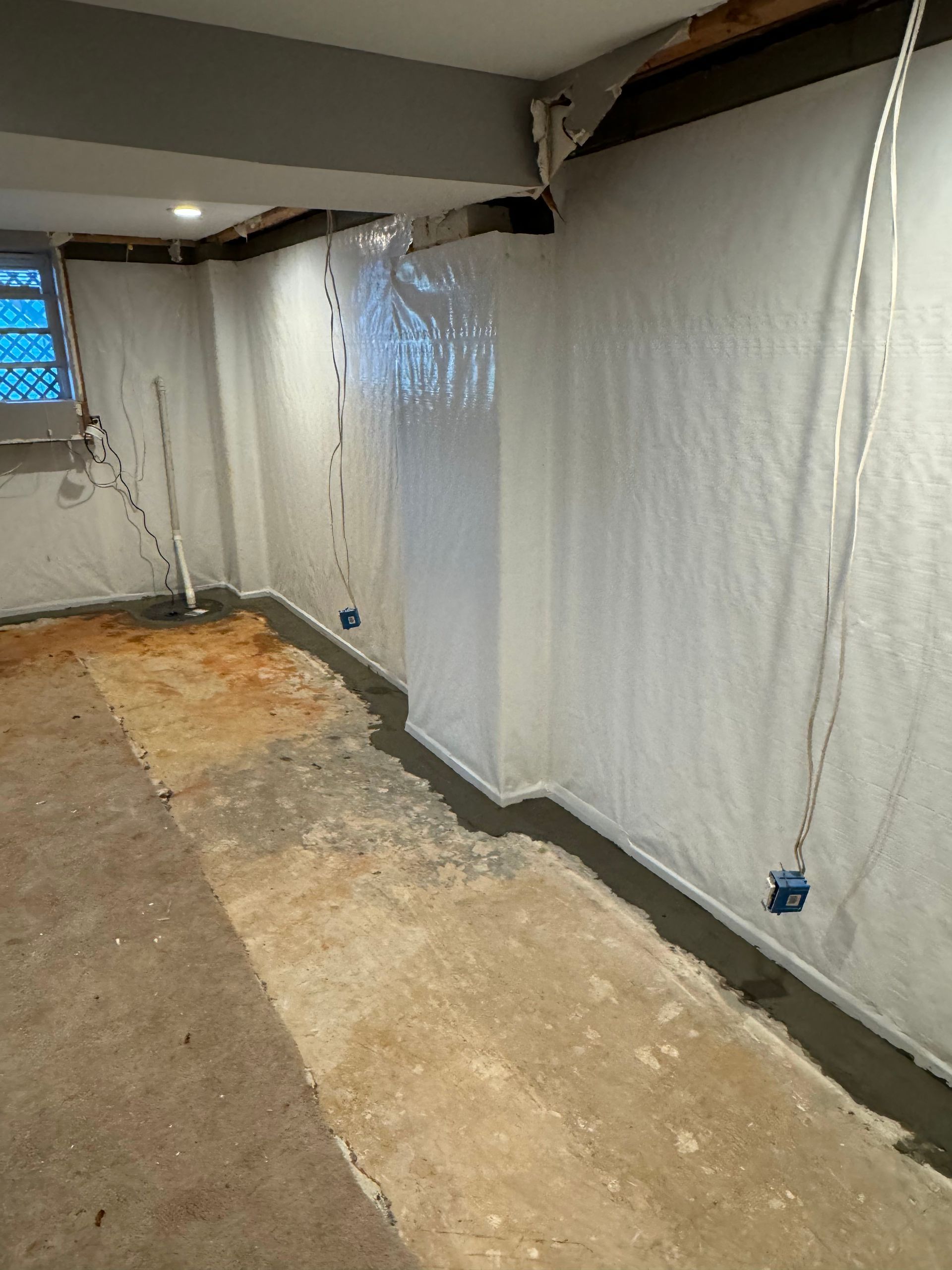 Basement under renovation with plastic sheeting on walls and a bare concrete floor