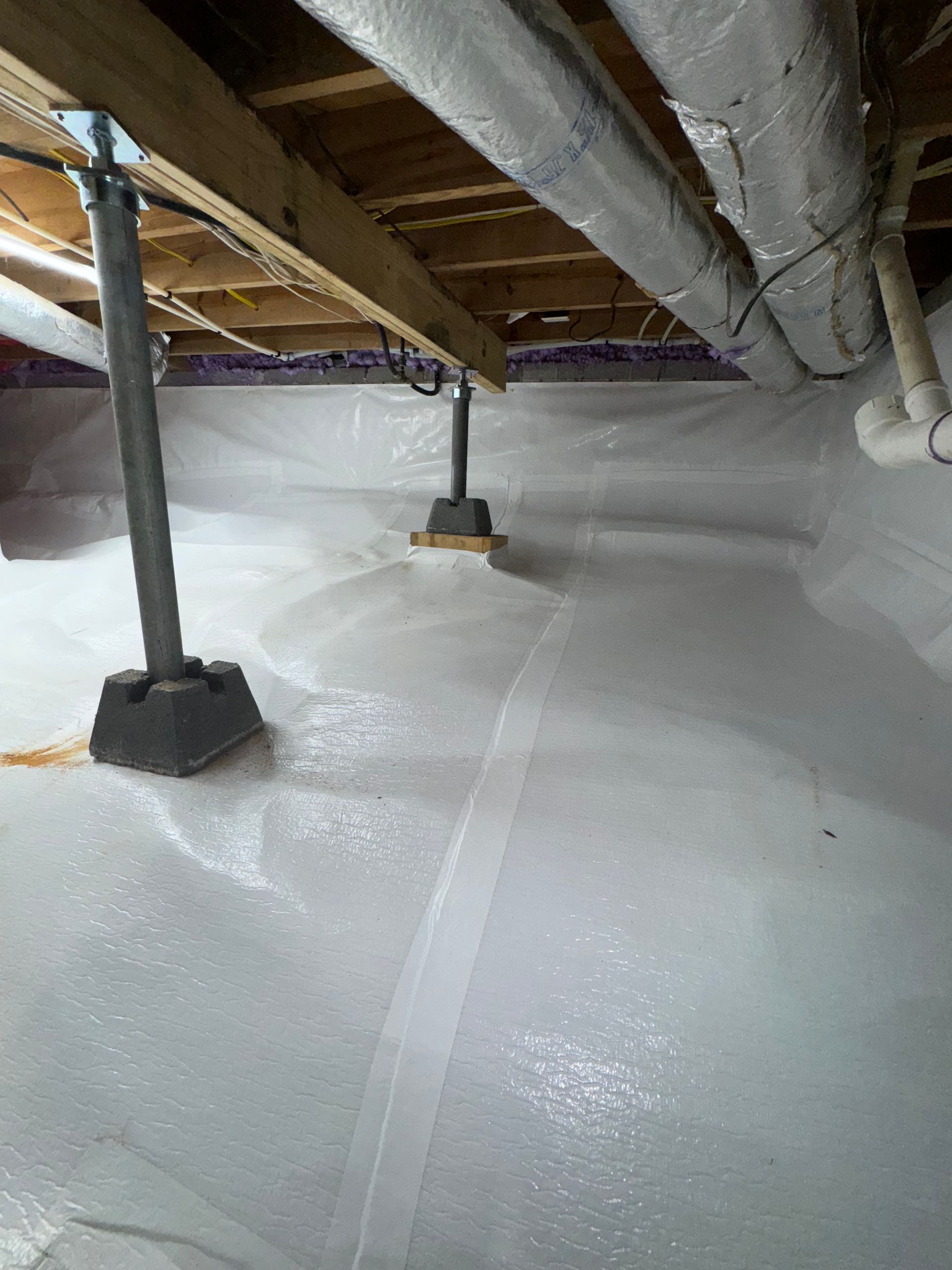 Crawlspace with insulated white floor, exposed wooden beams, pipes, and support posts.