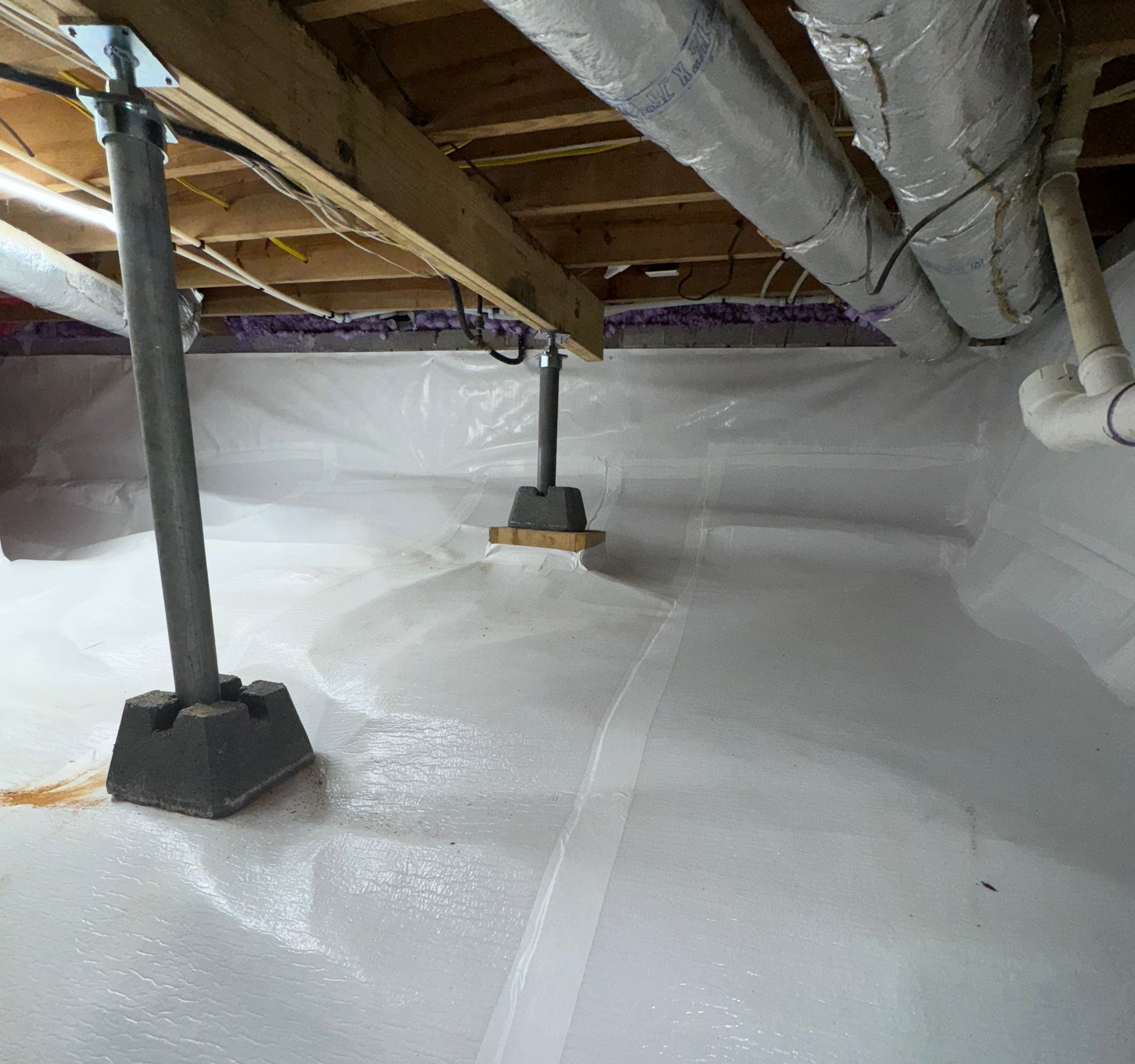 Crawlspace under floor joists with insulated ductwork, support posts, and white vapor barrier flooring.