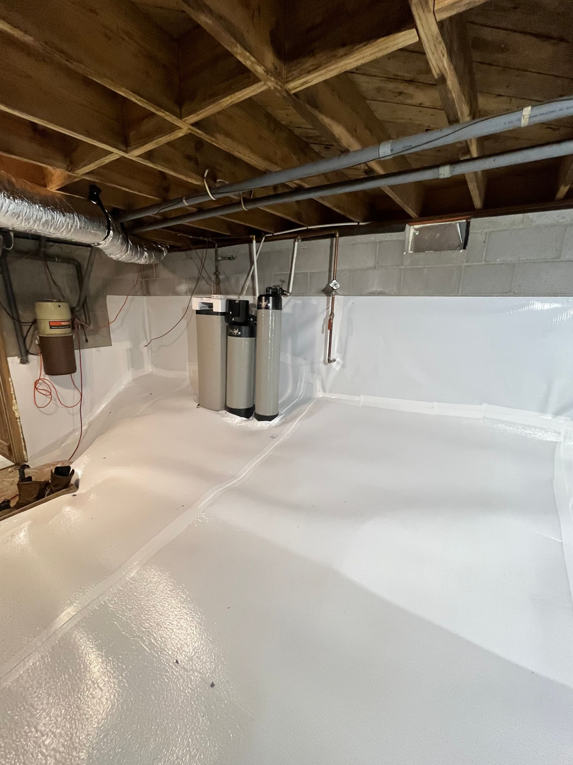 Basement utility room with bright white sealed floor, exposed joists, and water heater equipment