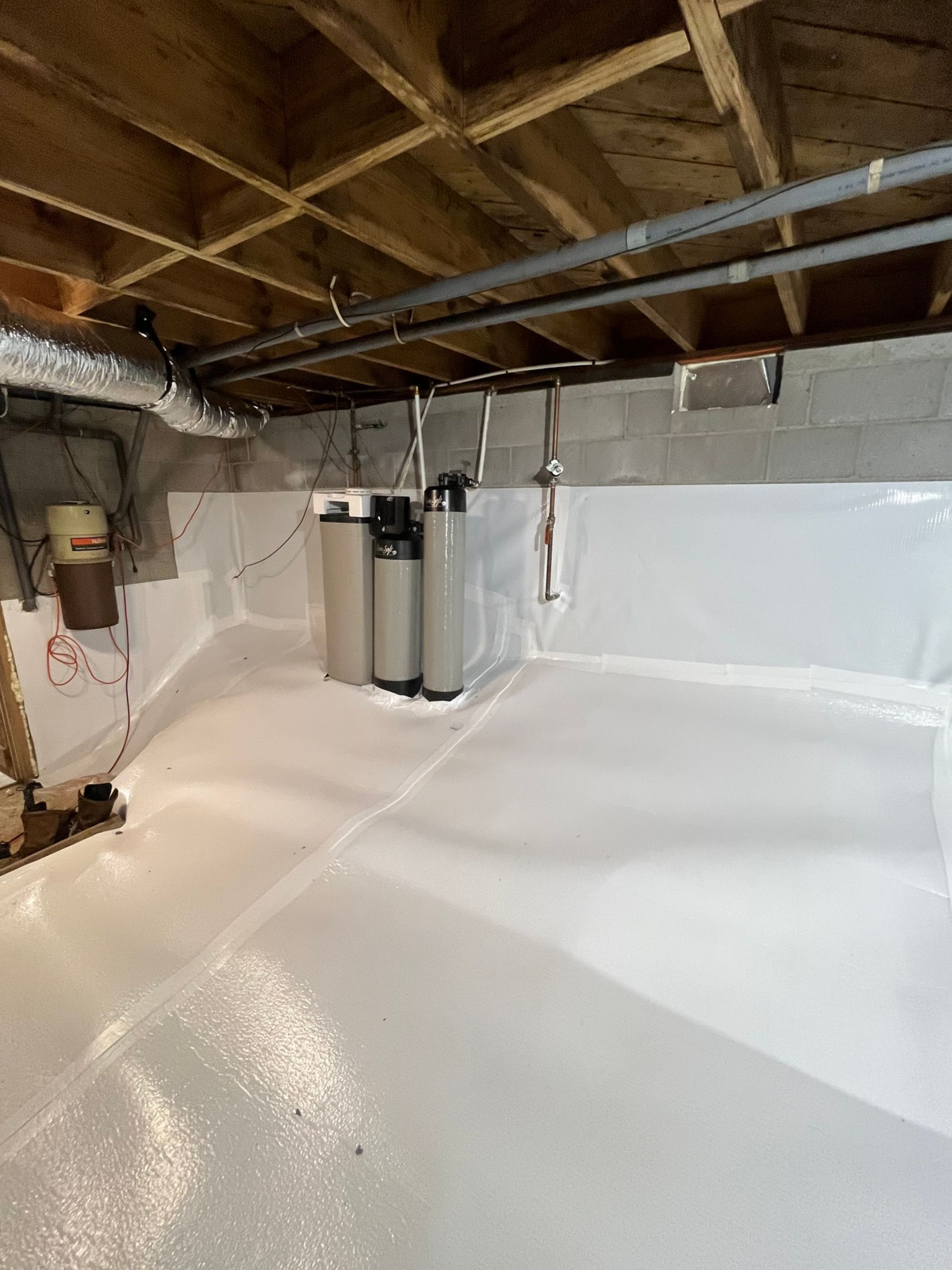 Basement interior with white plastic wall covering, electrical panel, sump pump, and exposed beams.