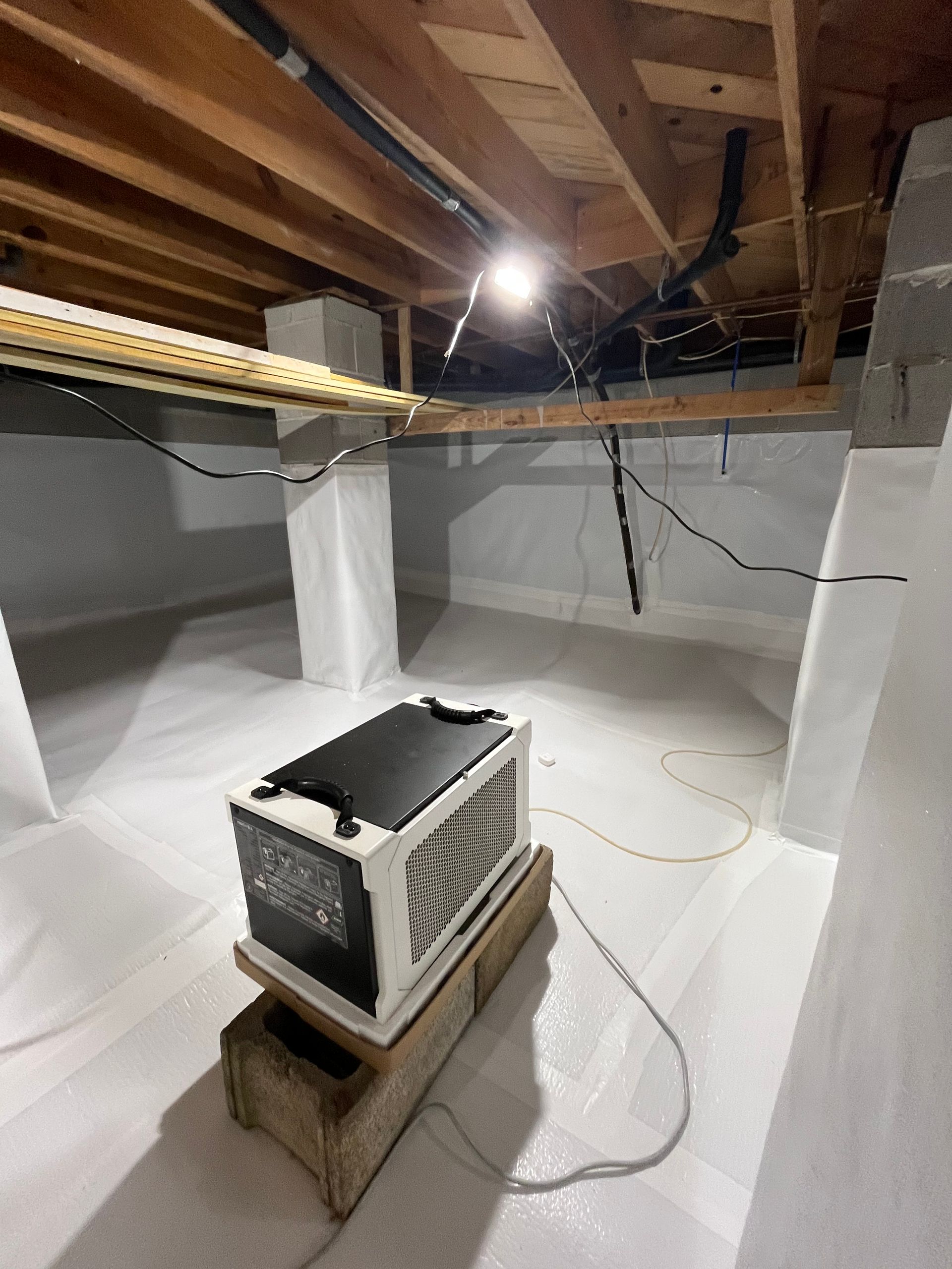 Basement with exposed beams, a furnace on a wooden crate, and white sheeting lining the walls.