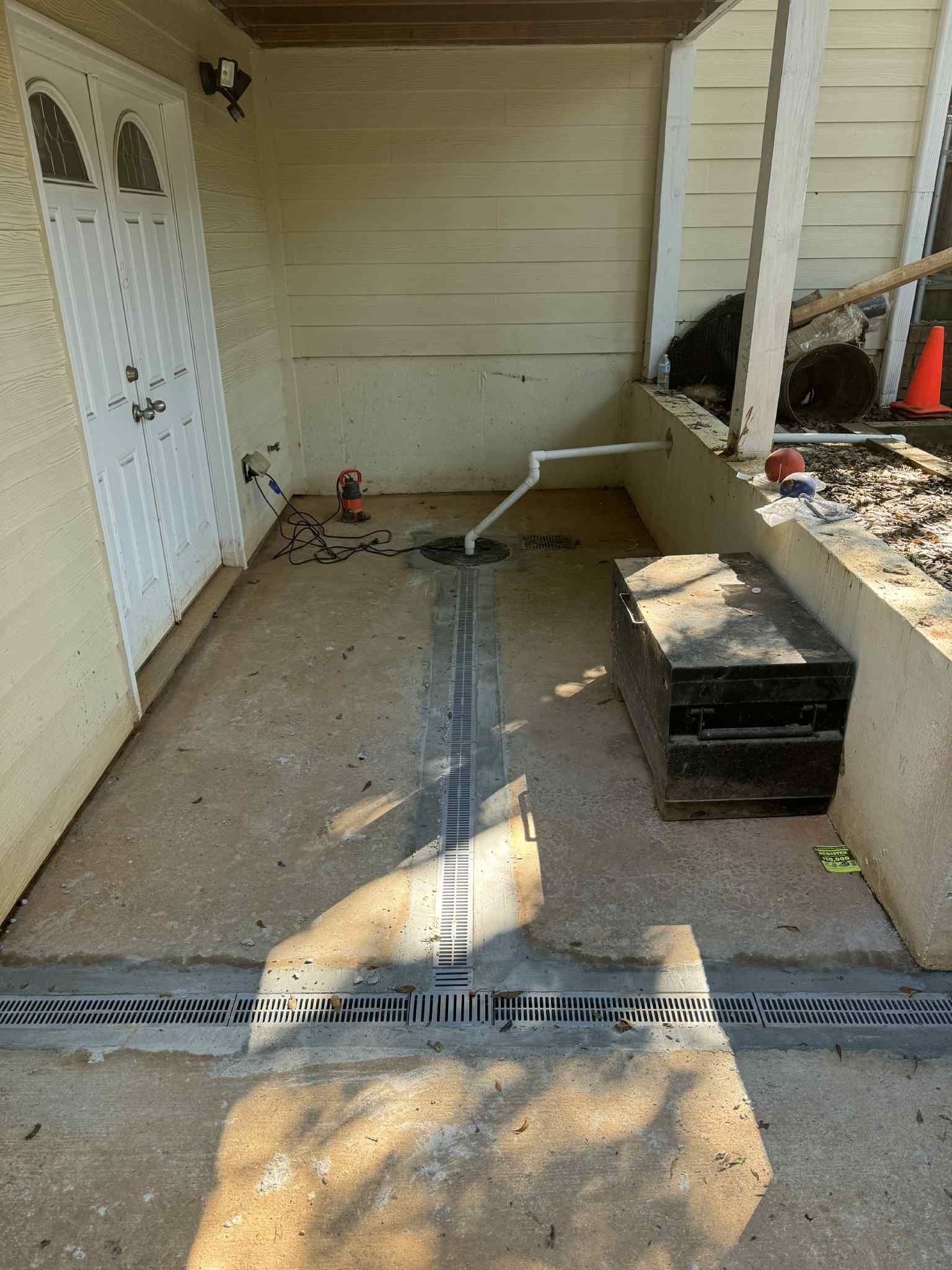 Narrow outdoor porch with white walls, concrete floor, drain grate, and a black storage box near the right side.