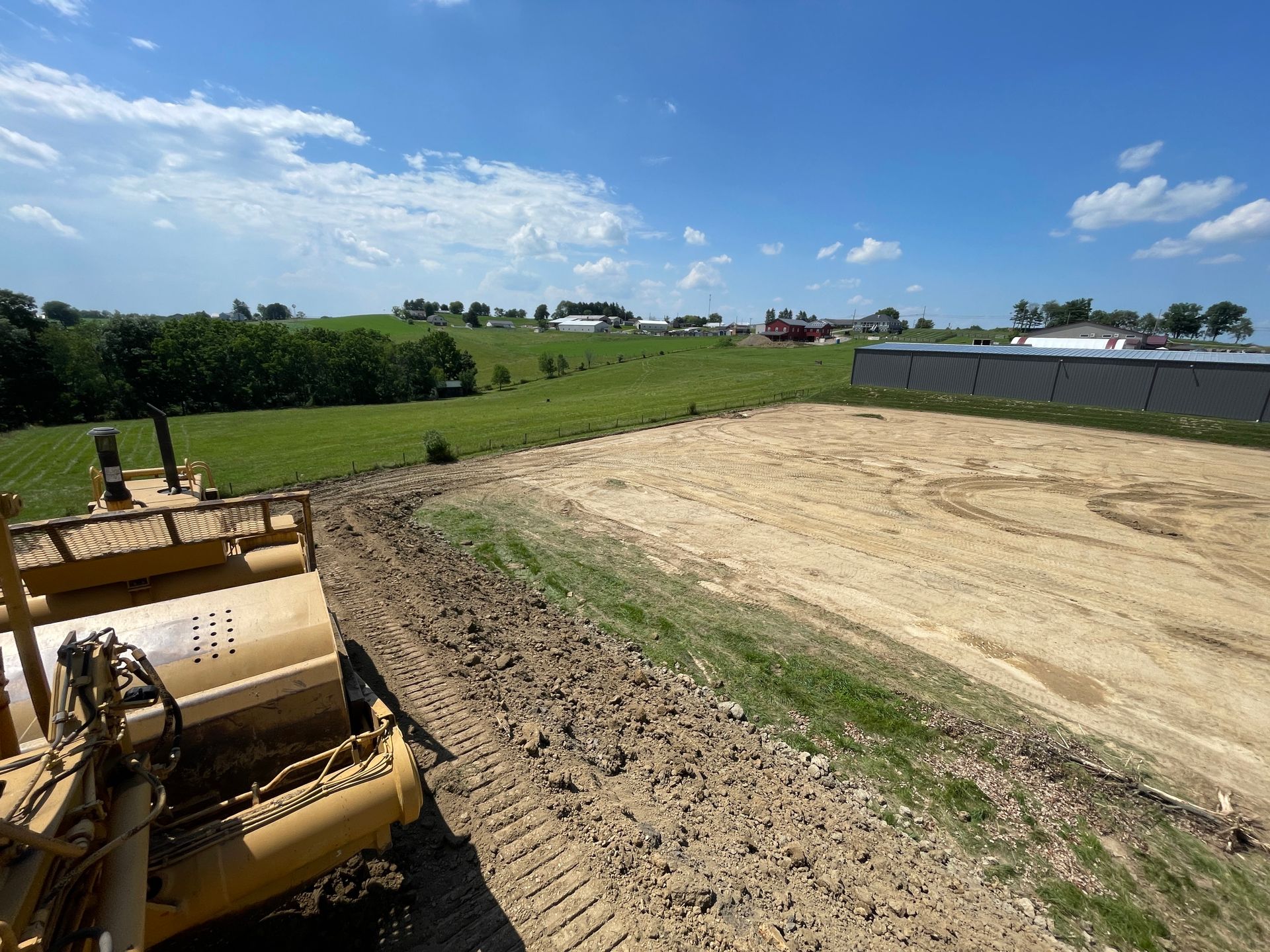 A yellow bulldozer leveling soil in a field on a sunny day.
