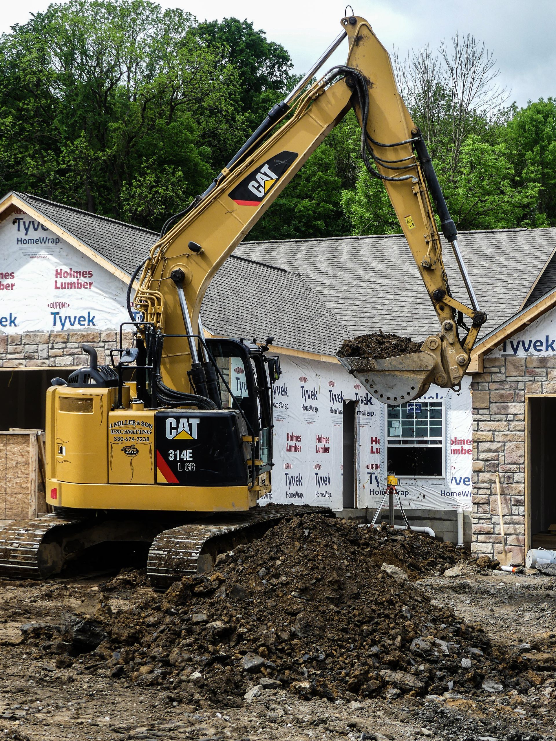Yellow CAT excavator digging dirt near a house under construction.